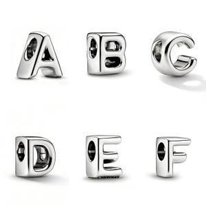 May include: Six silver alphabet charms, featuring the letters A, B, C, D, E, and F. Each charm is a three-dimensional design with a hole for stringing. The letters are in a sans-serif font.