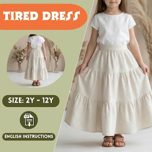 Può includere: Una ragazza indossa un top bianco a maniche corte e una gonna beige a balze. Il testo "TIRED DRESS" è arancione e "SIZE: 2Y - 12Y" è in un riquadro verde. L'immagine include anche il testo "ENGLISH INSTRUCTIONS".