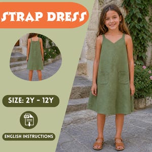 May include: Olive green strap dress with a V-neck and two front pockets. The image includes the text "STRAP DRESS", "SIZE: 2Y - 12Y", and "ENGLISH INSTRUCTIONS". A young person is wearing the dress. The dress is a casual style.