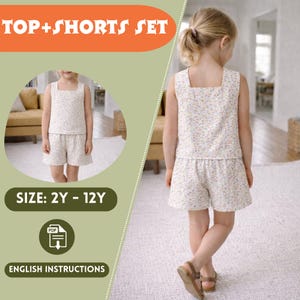 Puede incluir: Conjunto de dos piezas de top y shorts para niños. El conjunto presenta un top sin mangas con cuello cuadrado y shorts a juego, ambos en tela blanca con un delicado estampado floral. El texto "TOP+SHORTS SET" se muestra en la parte superior.
