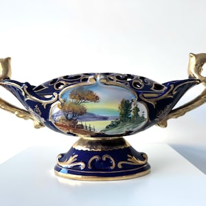 Könnte beinhalten: Dekorative ovale Porzellan-Mittelstückschale in Marineblau mit goldenen Griffen und Akzenten. Die Schale hat eine handgemalte Landschaftsszene und filigrane Details. Ein dekoratives Element für das Zuhause mit klassischem Design.