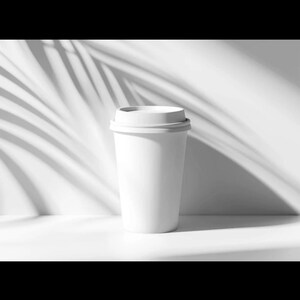 Könnte beinhalten: Ein weißer Einweg-Kaffeebecher mit Deckel, vor einem weißen Hintergrund mit Schatten von Palmblättern. Der Becher ist zylindrisch und scheint leer zu sein.