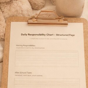 Könnte beinhalten: Ein Klemmbrett mit einem "Täglichen Verantwortungs-Chart" wird angezeigt, mit Abschnitten für Morgen- und Nachmittagsaufgaben sowie tägliche Reflexion. Ein beiger Teddybär und Bleistifte sind ebenfalls zu sehen.