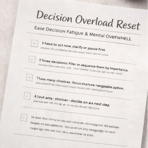 Könnte beinhalten: Ein weißes Blatt Papier mit dem Text "Decision Overload Reset" und einer Liste von Schritten zur Bewältigung von Entscheidungsermüdung. Eine Tasse Kaffee, ein Stift und eine Brille befinden sich ebenfalls auf der Oberfläche.