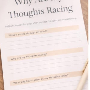 Könnte beinhalten: Eine Journalseite mit dem Titel „Warum rasen meine Gedanken?“ mit Aufforderungen zur Reflexion. Eine weiße Tasse mit einem Getränk und ein Stift liegen ebenfalls auf der Holzoberfläche. Das Journal enthält Fragen zu rasenden Gedanken und Emotionen.