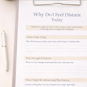 Peut inclure: Un presse-papiers avec une page de journal intitulée "Pourquoi je me sens distant aujourd'hui" et un stylo. Une tasse de café et des brins de fleurs blanches sont également dans l'image. Le journal invite à l'introspection.