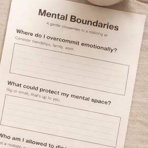 Könnte beinhalten: Eine weiße Tasse mit Kaffee steht neben einem Arbeitsblatt mit dem Titel "Mental Boundaries". Das Arbeitsblatt fordert den Benutzer auf, über emotionale Grenzen und den mentalen Raum nachzudenken. Der Hintergrund ist ein neutrales Beige.