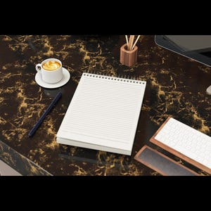 Könnte beinhalten: Eine Büroszene mit einem weißen Notizblock, einer Tasse Kaffee, einem Stift und einer Holz-Tastatur auf einer dunkelbraunen, marmorierten Oberfläche. Die Gegenstände deuten auf eine moderne Büro- oder Home-Office-Umgebung hin, mit dem Notizblock zum Notieren.