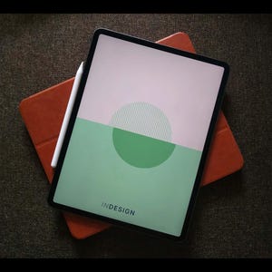Op de afbeelding: Een digitale tablet met een witte stylus rust op een oranje tabletcase. Het tabletscherm toont een ontwerp met een groen en roze kleurblok en het woord "INDESIGN".