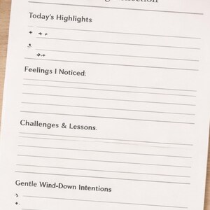 Könnte beinhalten: Eine Journalseite mit der Überschrift „Abendliche Reflexion“ mit Aufforderungen zur täglichen Reflexion. Die Seite enthält Abschnitte für „Highlights des Tages“, „Gefühle, die ich bemerkt habe“ und „Herausforderungen & Lektionen“. Eine Tasse Kaffee und ein Stift sind ebenfalls sichtbar.