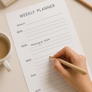 Könnte beinhalten: Ein weißer Wochenplaner mit dem Titel "WEEKLY PLANNER". Der Planer hat Linien für jeden Wochentag. Eine Hand schreibt "Meeting at 10 AM" mit einem beigen Stift. Ein beiger Bleistift und ein beiges Notizbuch sind ebenfalls sichtbar.