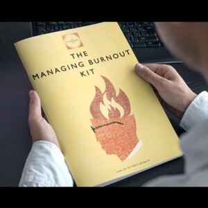 May include: A yellow booklet titled "THE MANAGING BURNOUT KIT" is held by a person. The cover features a stylized illustration of a head with flames, suggesting stress management. The booklet's design is simple and professional.