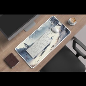 Può includere: Un'impostazione da scrivania per computer con tastiera bianca, mouse e tappetino per mouse a tema paesaggio. Sono visibili anche un monitor, un piccolo taccuino marrone e una tazza di caffè. La scrivania è in legno.