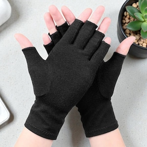 Pode incluir: Luvas pretas sem dedos. Estas luvas cobrem a mão até às articulações, com aberturas para os dedos e o polegar. Feitas de um tecido escuro e macio, oferecem calor e flexibilidade.