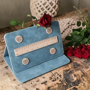 May include: A light blue tablet case with a wooden ruler and four heart-shaped magnets. A red rose is placed on top of the case. The ruler measures up to 20 inches. The case is open and resting on a wooden surface.