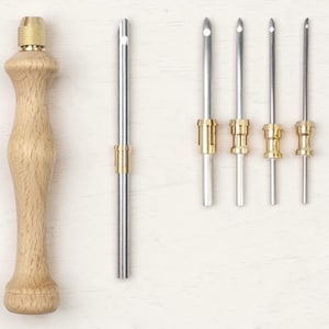 May include: A wooden punch needle tool with a brass tip and handle, alongside four additional needles with brass and silver components. The tools are designed for embroidery and punch needle crafts.
