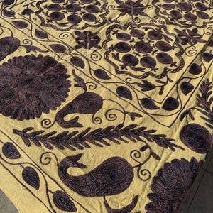 Peut inclure: Gros plan sur un textile jaune avec des broderies complexes violet foncé. Le motif présente des motifs floraux et cachemire, avec des fleurs stylisées, des feuilles et des lignes courbes. Le tissu est plié, montrant la texture et la profondeur de la broderie.