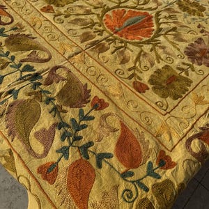 Peut inclure: Textile brodé aux couleurs jaune, orange, vert et marron. Le motif présente des motifs floraux et cachemire, avec une bordure à motifs répétitifs. Le tissu semble doux et est drapé.