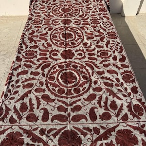 Peut inclure: Textile brodé blanc et bordeaux avec un motif floral et cachemire. Le textile est étalé, mettant en valeur le design complexe et les coutures détaillées. La palette de couleurs est une combinaison de blanc et de rouge foncé.