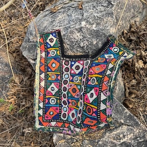 Könnte beinhalten: Ein farbenfrohes, besticktes Textil mit geometrischen Mustern und Spiegelakzenten. Das Stück hat einen schwarzen Rand und eine Vielzahl von leuchtenden Farben, darunter Rosa, Orange, Blau und Grün. Das Textil ist wahrscheinlich ein Dekorationsartikel oder Teil eines Kleidungsstücks.