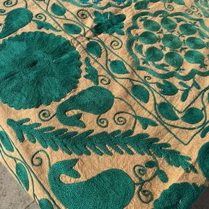 Peut inclure: Gros plan sur un textile avec une broderie vert émeraude complexe sur un fond beige. Le motif présente des motifs floraux et cachemire, avec des coutures détaillées et un aspect texturé. Le tissu a une texture légèrement froissée.