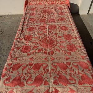 Peut inclure: Textile beige avec broderies florales rouges complexes. Le motif présente de grandes fleurs, des formes de type cachemire et des motifs enroulés. Le textile est probablement une couverture de lit décorative ou une tenture murale.