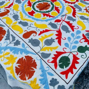 Peut inclure: Textile blanc avec broderies complexes de différentes couleurs. Le motif présente des motifs floraux et cachemire en rouge, jaune, bleu, orange et gris. Les bords sont finis avec un ourlet simple.
