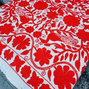 Peut inclure: Textile blanc avec une broderie rouge vif représentant des fleurs et des oiseaux. Le motif complexe présente des fleurs, des feuilles et des oiseaux stylisés, créant une esthétique détaillée et attrayante. Les bords sont finis avec une bordure décorative.