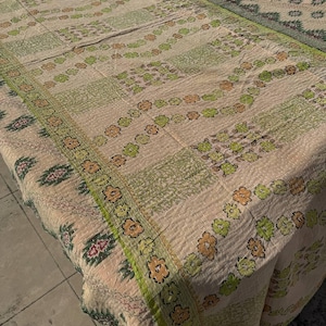 Peut inclure: Une courtepointe beige et verte à motifs floraux et géométriques. La courtepointe présente un motif répétitif de fleurs et de feuilles dans des tons de vert et d'orange, avec une bordure verte. La courtepointe est faite d'un tissu doux et texturé.