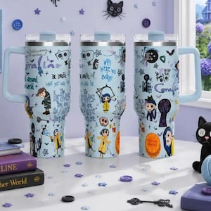 May include: Three light blue stainless steel tumblers with handles and clear lids, featuring a wrap-around graphic print of Coraline characters, buttons, keys, and text including "Coraline," "Be Careful," and "Why Were You Born?" in various fonts.