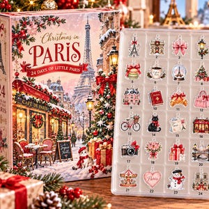 May include: A Christmas in Paris advent calendar box featuring a Parisian street scene with the Eiffel Tower and a clear plastic tray containing 24 numbered acrylic ornaments including a cat, a croissant, a camera, and a snowman.