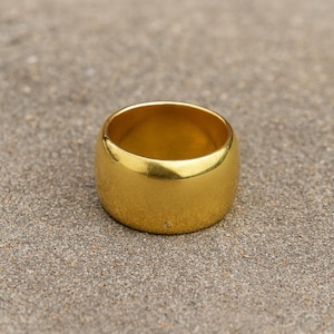 Peut inclure: Une bague dorée de forme cylindrique arrondie. La bague a une surface lisse et polie et un design simple. La bague est un bijou.