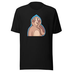Puede incluir: Camiseta negra con una ilustración de un mono de dibujos animados. El mono es de color marrón claro con un contorno azul, tocándose el dedo en la boca en una pose pensativa. La camiseta está hecha de un material suave.