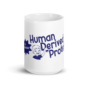 May include: White ceramic mug with a blue graphic that reads "Human Derived Protein." The design includes a cartoon illustration of a smiling boy holding a carton of milk. The text "It's gettable!" is also included.