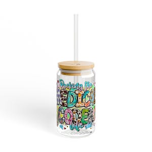 Puede incluir: Un vaso de vidrio transparente con tapa de bambú y pajita transparente. El vaso está decorado con texto colorido que dice "Rocking the MEDICAL CODER life". El diseño incluye corazones, guantes médicos y un estampado de vaca.