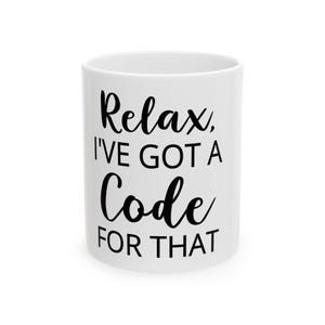 Może przedstawiać: Biały ceramiczny kubek z napisem "Relax, I've got a Code for That" czarnym pismem. Kubek jest cylindryczny i wydaje się pusty. Tekst jest wyśrodkowany na kubku.
