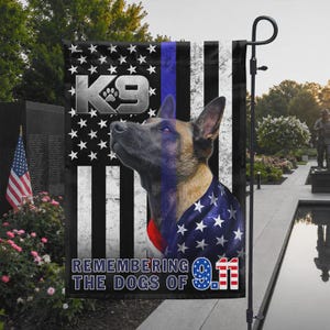 May include: A rectangular garden flag featuring a Belgian Malinois dog portrait against a black and white American flag background with a vertical blue stripe. The text K9 and REMEMBERING THE DOGS OF 9.11 are printed in bold white lettering.