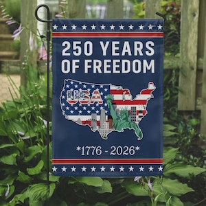 Puede incluir: Una bandera de jardín azul con el texto "250 YEARS OF FREEDOM" en blanco. La bandera presenta un mapa de los EE. UU. con la Estatua de la Libertad y un paisaje urbano. La bandera también incluye los años "1776-2026" y estrellas.