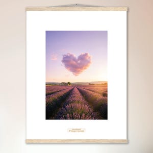 Op de afbeelding: Een ingelijste print met een lavendelveld bij zonsondergang en een hartvormige wolk. De print wordt getoond met een houten hanger. De afbeelding heeft een warme, romantische uitstraling.