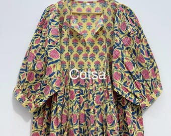 May include: A yellow dress with a floral pattern in pink and blue. The dress has long, puffy sleeves and a V-neckline. The text "Cotsa" is printed on the front of the dress.