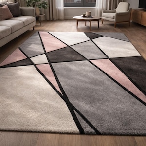Peut inclure: Tapis rectangulaire à motifs géométriques dans les tons de gris, rose et noir. Le tapis présente un design moderne avec des formes et des lignes angulaires. Il semble être fait d'une matière douce, idéal pour un salon, mesurant environ 200 cm x 300 cm.