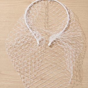 May include: A white bridal veil with a net design. The veil is attached to a white headband. The netting is a diamond pattern. The veil is made of a lightweight material.