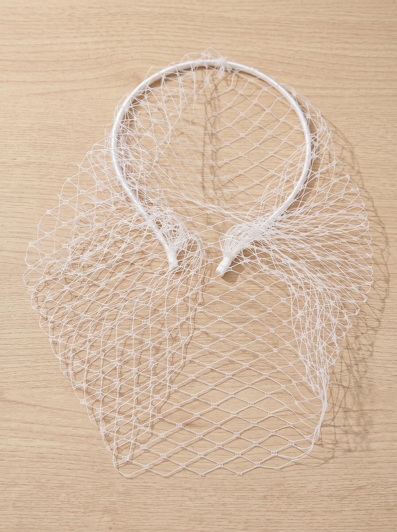 May include: A white bridal veil with a net design. The veil is attached to a white headband. The netting is a diamond pattern. The veil is made of a lightweight material.