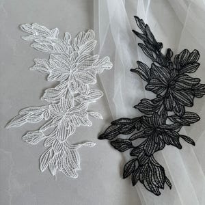 May include: Two floral lace appliques. One is white, the other is black. Each applique features a detailed, openwork design of flowers and leaves. The appliques are likely for embellishing garments or crafts, adding a delicate, elegant touch.