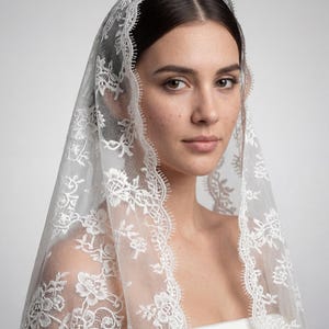 May include: A white, delicate lace veil with floral patterns and a scalloped edge. The veil is draped over a person's head and shoulders, creating a soft, romantic look. The intricate lace design adds a touch of elegance, perfect for bridal wear.