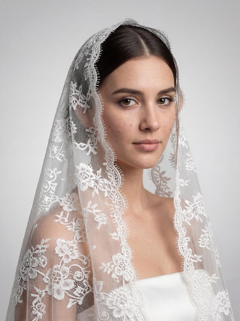 May include: A white, delicate lace veil with floral patterns and a scalloped edge. The veil is draped over a person's head and shoulders, creating a soft, romantic look. The intricate lace design adds a touch of elegance, perfect for bridal wear.