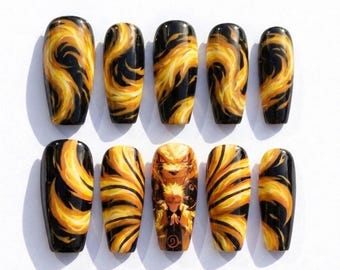 May include: A set of ten press-on nails featuring a black background with swirling yellow and orange flame-like patterns. One nail displays a detailed illustration of a character with spiky blonde hair and a large fox face behind them.
