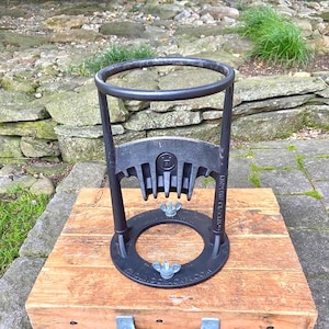 May include: A black Kindling Cracker wood splitter with a round top and a circular base, mounted on a wooden box with a metal handle. The splitter has a distinctive design with a blade and a ring for holding wood.