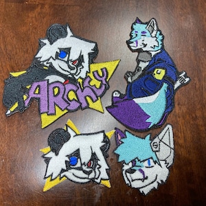 May include: Four embroidered patches featuring anthropomorphic animal characters. One patch has the word "ARCHY" in purple letters. The patches are in various colours, including black, white, blue, purple, and yellow.