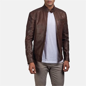 May include: A brown leather jacket with a stand-up collar and a zip closure. The jacket has a slim fit and features a chest pocket and quilted detailing on the shoulders and sleeves. The model is wearing a white t-shirt and grey trousers.